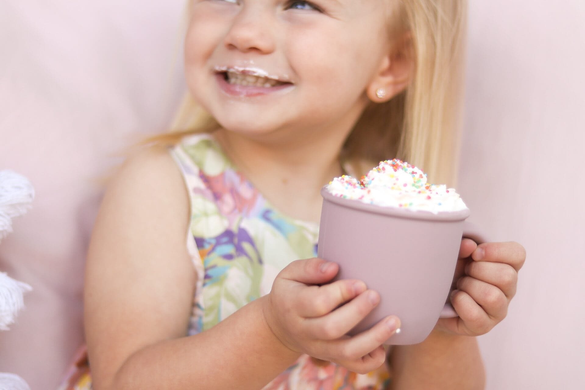 Blonde haired girl smiling drinking a babychino from a pink mug. she has a milk moustache